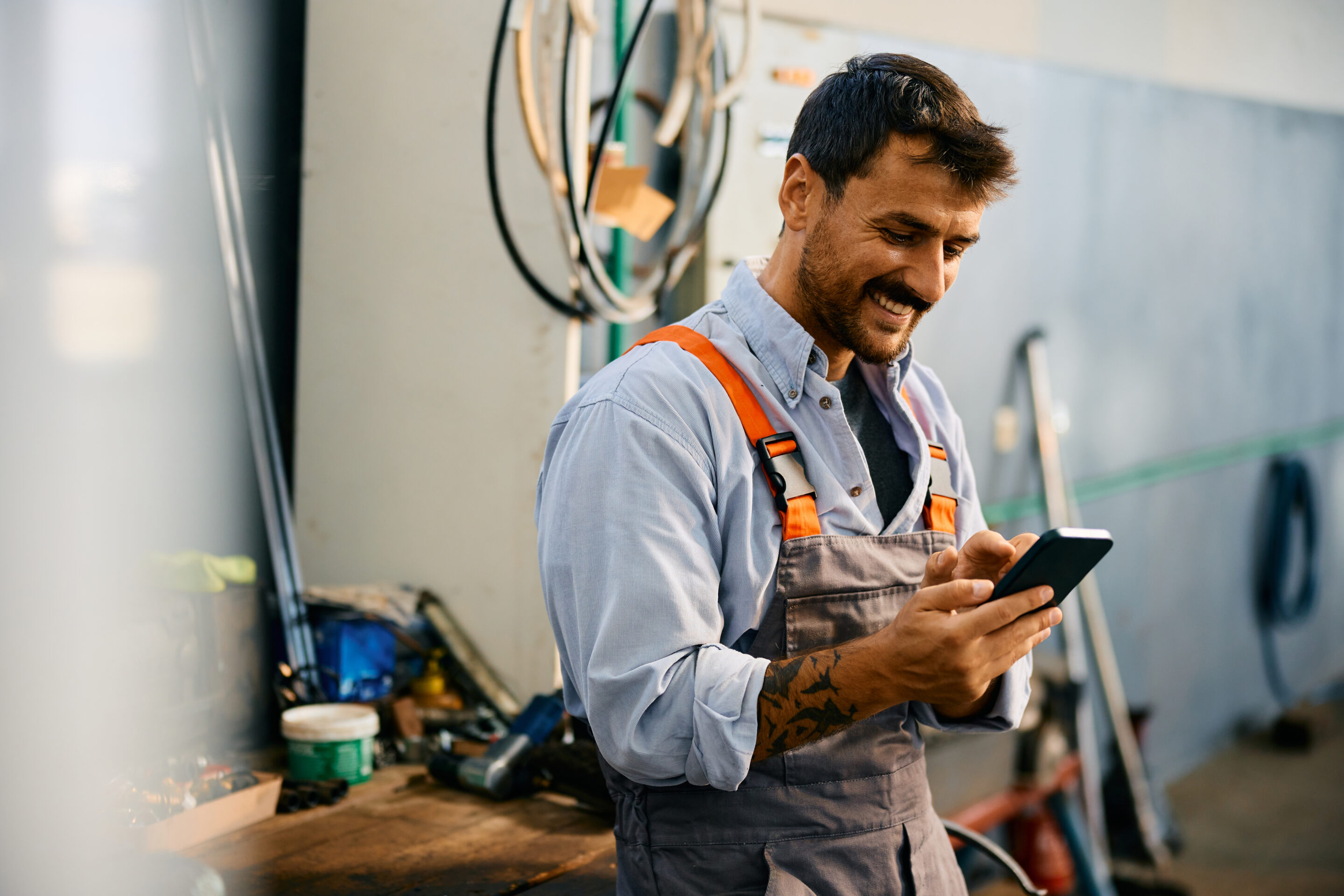 Happy mechanic using smart phone while working in a repair shop.